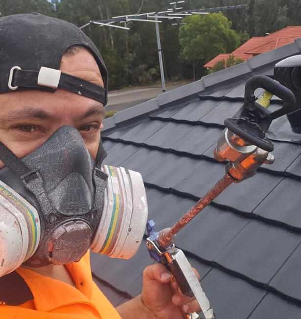 Klean Kingdom director on the roof spray-applying premium roof membrane in Mount Annan, Sydney — hands-on roof restoration, no subcontractors, every job done personally Klean Kingdom owner spray painting a concrete tile roof with respirator and full PPE during a roof restoration job in Mount Annan, Sydney